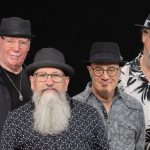 Bottleneck Blues Band group photo - four members dressed in black and white on a black background