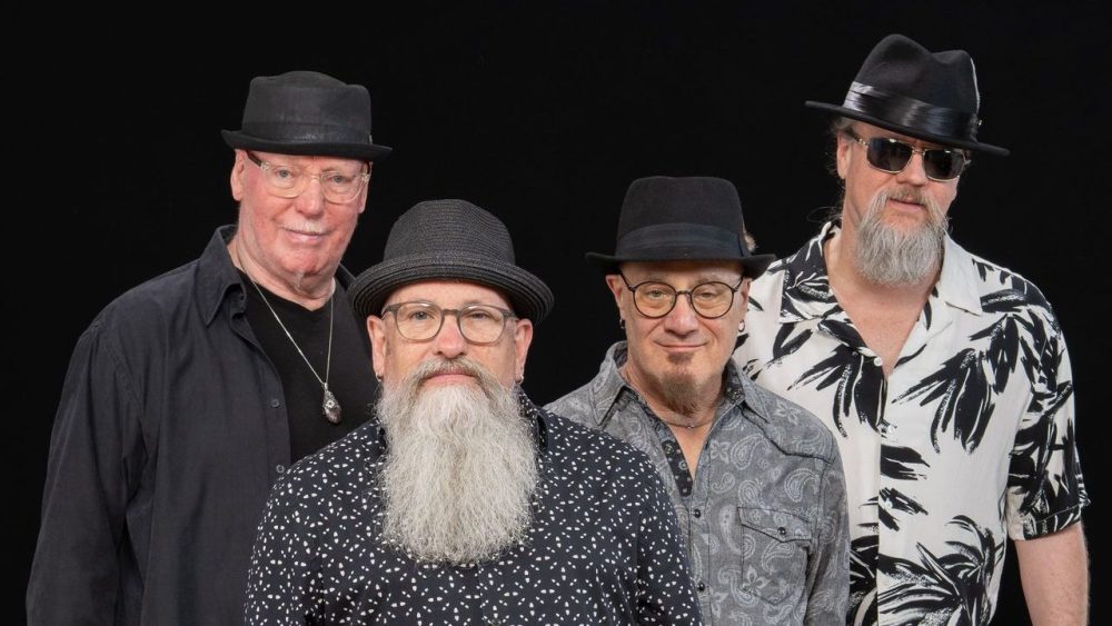 Bottleneck Blues Band group photo - four members dressed in black and white on a black background